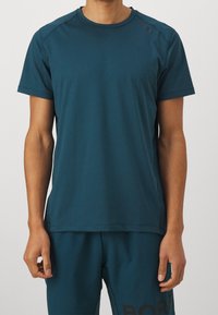 Tyrkysové sportovní tričko s krátkými rukávy, kulatým výstřihem a jemným logem na jednom rameni. Hladká textura a přiléhavý střih.