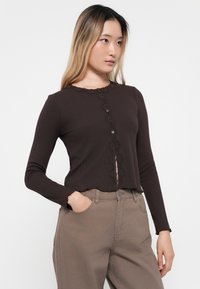 Brun ribbet langermet topp med blonder langs halslinjen og knappelukking, med en kort design og bølget kant.