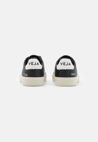Sneaker nere in pelle con linguette bianche sul tallone, caratterizzate dal marchio "VEJA". Forma arrotondata e suole in gomma di colore chiaro. Texture liscia.