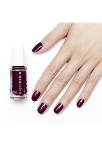 Diep paarse nagellak in een glazen fles met een witte dop, naast een hand met gemaakte nagels die in dezelfde kleur zijn geverfd.