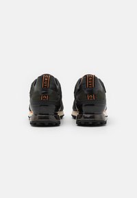 Baskets de sport noires avec une tige texturée, des accents orange et un talon noir brillant. Dotées d'une semelle durable pour l'amorti et l'adhérence.