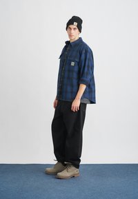 Μπλε και μαύρο καρό πουκάμισο φλις, γκρι ριγέ μπλούζα από κάτω, μαύρο φαρδύ παντελόνι και γκρι μπότες με καφέ σόλες, μαύρο σκουφί.