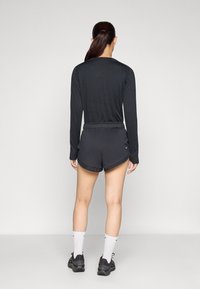 Pitkähihainen musta paita pyöreällä kaula-aukolla, yhdistetty mustiin shortseihin. Molemmat vaatteet ovat valmistettu kevyestä, hengittävästä kankaasta. Mustat lenkkarit ja valkoiset sukat.