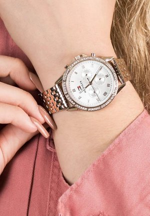 Montre argentée avec chiffres romains, trois sous-cadrans et un cadran orné de cristaux. Équipée d'un bracelet en maille dorée rose et d'un cadran blanc.