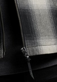 Karo-Gewebejacke in Schwarz und Weiß, mit durchgehendem Reißverschluss und schwarzer Hardware. Strukturmuster mit markantem Fischgrät-Design.