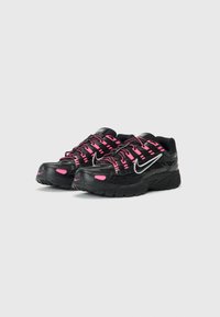 Schwarze Sport Schuhe mit rosa Akzenten, ausgestattet mit einem strukturierten Obermaterial, schwarzen Schnürsenkeln, einer gepolsterten Sohle und einem silbernen Nike-Logo an der Seite.