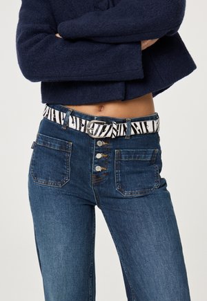 Die Denim-Jeans haben ein tailliertes Design mit einer dunkelblauen Waschung, fünf Taschen und einem gemusterten schwarz-weißen Gürtel mit einer silbernen Schnalle.