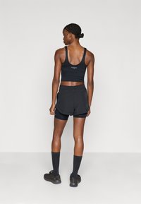 Top deportivo negro corto con tirantes anchos y detalle de logo, combinado con pantalones cortos negros en capas. El conjunto presenta una textura de tela suave.