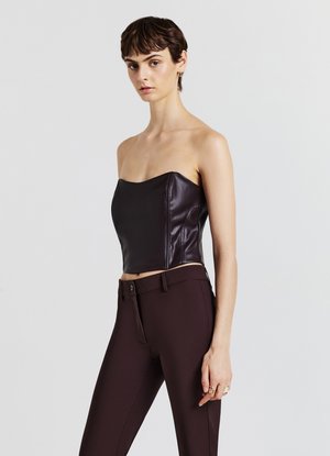 Crop top sans manches en cuir noir avec un design ajusté et une texture lisse, associé à un pantalon ajusté marron foncé.