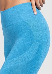 Leggings sportivi blu con un tessuto liscio e texture, vita alta e un dettaglio a cucitura curvata lungo i lati.