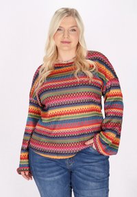 Buntgestreifter Pullover mit lebendigen Zickzack- und geometrischen Mustern, aus einem strukturierten Strickstoff und mit langen Ärmeln. Kombiniert mit Jeans.