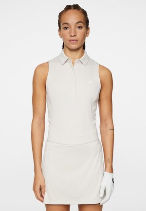 Abito polo senza maniche di un beige chiaro con un colletto, vita aderente e una texture liscia. Indossato con un guanto da golf bianco.
