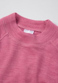 Lähikuva vaaleanpunaisesta pyöreäkaula-aukollisesta villapaidasta, jossa näkyy neuleen rakenne, kaksoisompeleet ja tyhjät valkoiset tarrat kauluksessa.