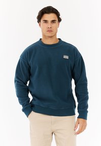 Blauwe fleece sweatshirt met een ronde hals, ribbels aan de mouwen en onderkant, voorzien van een klein logo op de linker borst. Gladde textuur.
