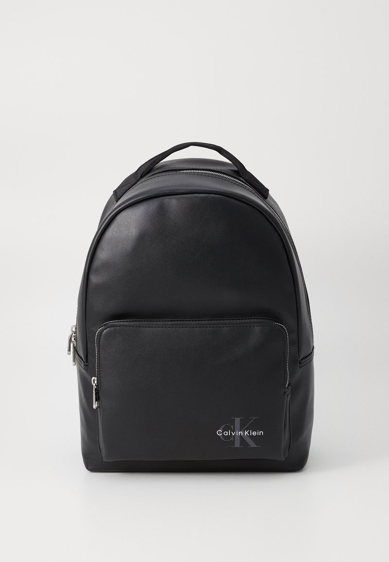 Mochila preta feita de faux leather suave. Apresenta uma forma arredondada, bolso frontal com fecho e um pequeno logótipo na parte inferior da frente.