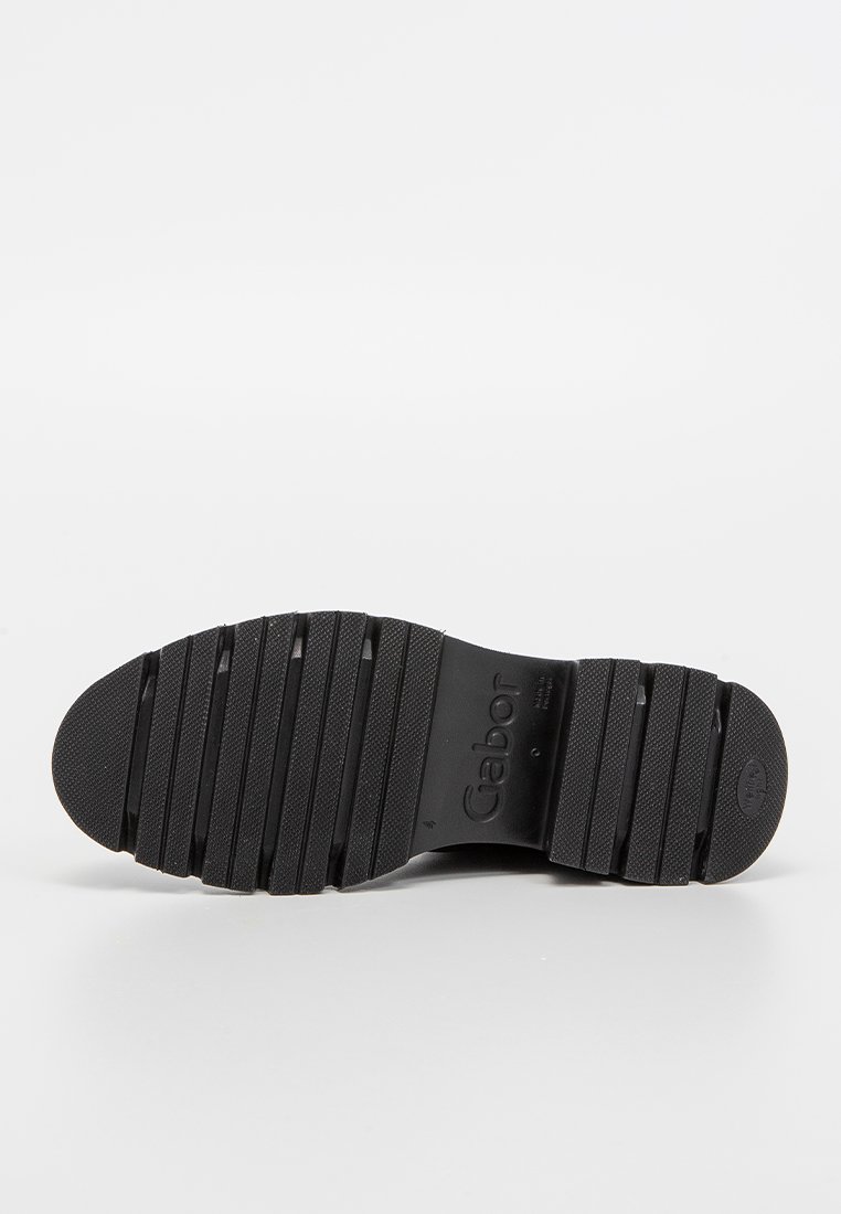 Suela de zapato de goma negra con agarre texturizado y ranuras horizontales. Presenta marca y punta redonda. Superficie lisa y plana con leve arco.