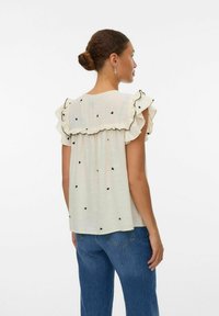 Blouse en crème clair avec motif de cœurs noirs, manches volantées et bordures contrastantes. Tissu doux, coupe décontractée et détail de pli au dos.