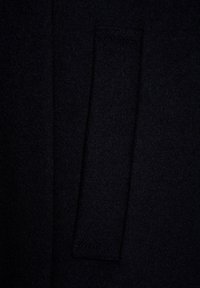 Czarna wełniana tkanina pokazująca zbliżenie kieszeni z gładką teksturą i starannie wykończonym szwem. Tkanina ma bogaty, głęboki kolor.