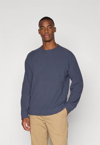 Mørkeblå sweatshirt med lange ærmer, rund hals og raglan-sømme. Lavet af blødt materiale med en let struktur og en diskret logodetalje.