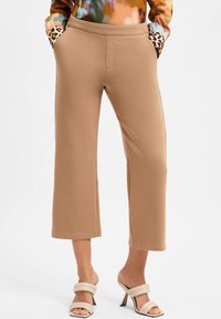 Beige cropped pants with soft texture, featuring slip pockets trimmed in leopard pattern; paired with neutral strappy high-heeled sandals.