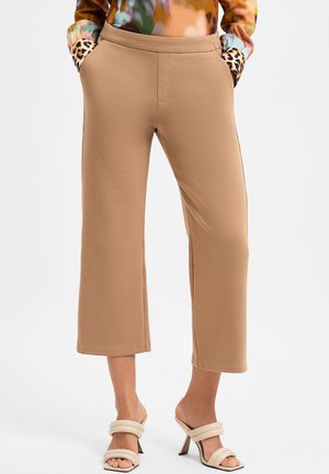 Beige cropped broek met een zachte textuur, voorzien van insteekzakken afgewerkt met een luipaardpatroon; gecombineerd met neutrale strappy hoge hakken.