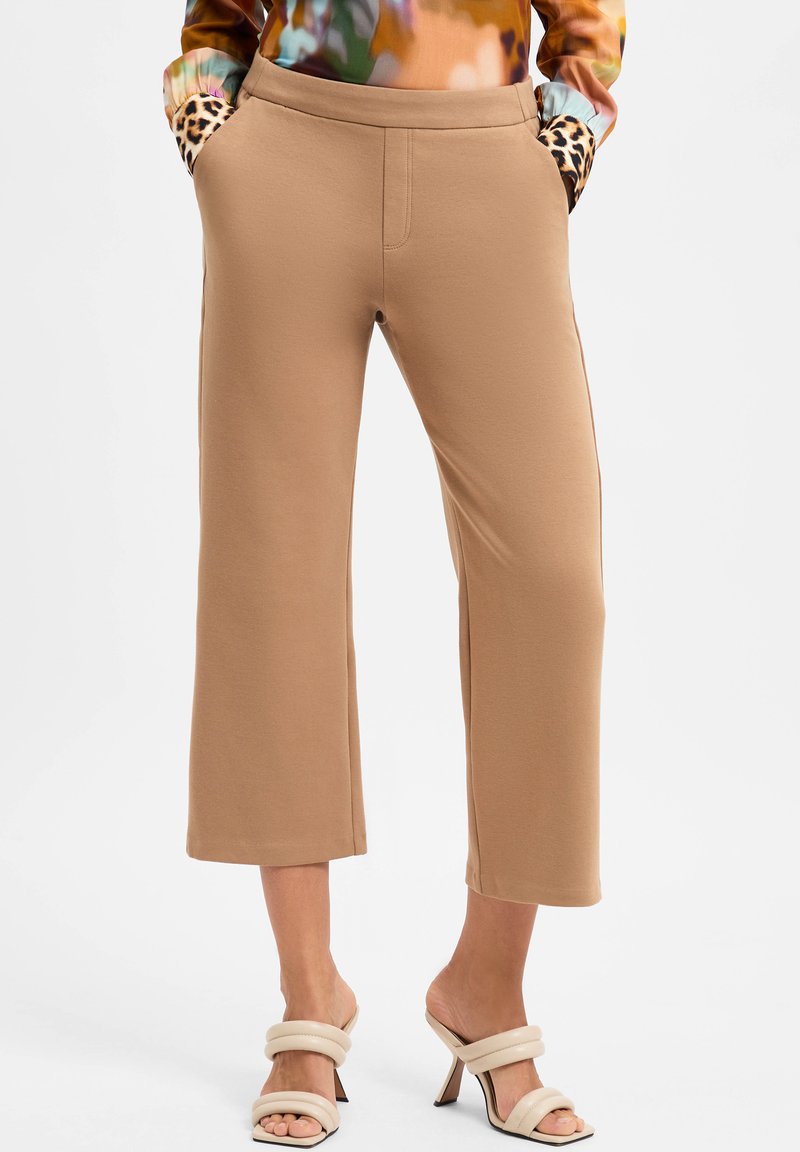 Beige cropped pants with soft texture, featuring slip pockets trimmed in leopard pattern; paired with neutral strappy high-heeled sandals.