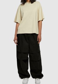 Camiseta beige de gran tamaño con mangas cortas, combinada con pantalones cargo negros holgados que tienen grandes bolsillos, usados con zapatillas blancas.