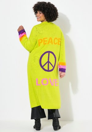 Pull long vert vif avec le texte "PAIX" et "AMOUR" en orange et rose, mettant en avant des accents violets sur les manches et un symbole de paix.