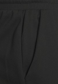 Zwarte broek van textuurstof, met geplooide voorkant en een elastische tailleband voor een verstelbare pasvorm.