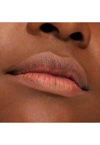 Zbliżenie na usta o ciemnym odcieniu skóry. Usta są lekko rozchylone, ukazując naturalny beżowy odcień. Tekstura skóry jest gładka z delikatnymi, subtelnymi liniami.