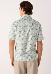 Camisa de manga corta de algodón en verde claro con un estampado floral, con detalles en azul y blanco. Cuello estándar y corte relajado.