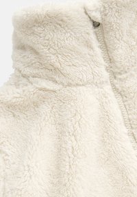 Cremefarbene Fleecejacke aus strukturiertem, flauschigem Material. Verfügt über einen Reißverschluss und einen hohen Kragen für zusätzlichen Wärme.