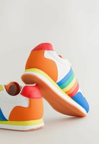 Pari värikkäitä lenkkareita, joissa on oransseja, sinisiä, vihreitä, keltaisia ja punaisia yksityiskohtia, valkoista kangasta ja kuvioidut kumipohjat vaalealla taustalla.