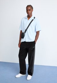 Light blue textured short-sleeve shirt, black corduroy pants with side stripes, black crossbody bag, and white sneakers.