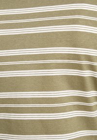 Camisa de algodão com tecido verde-oliva e riscas brancas horizontais de larguras variadas, textura suave e um acabamento lisinho.