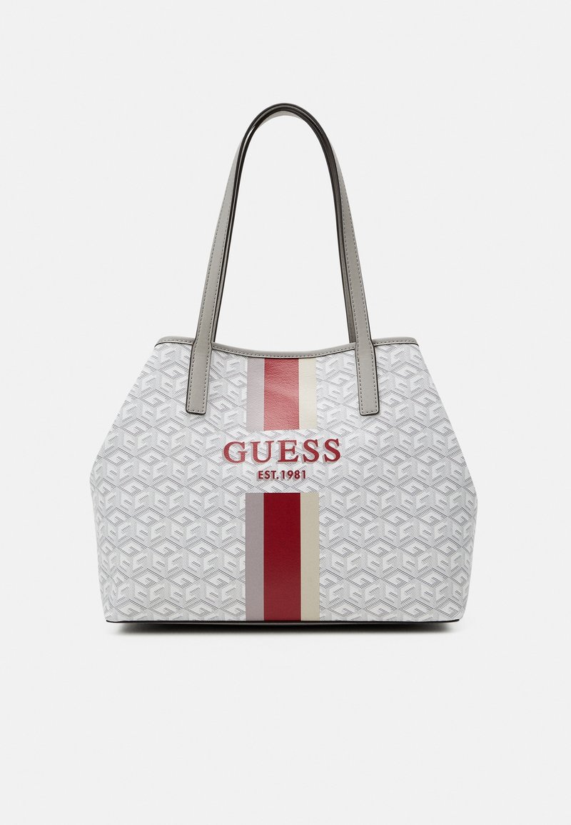 Sac fourre-tout blanc Guess avec motif gris, rayures verticales rouges et beiges, texte du logo rouge et doubles poignées grises.