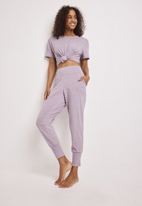 Lichtpaarse cropped t-shirt met een knoop vooraan en korte mouwen, gecombineerd met bijpassende losse joggers met zijzakken.