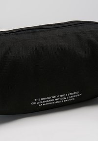 Black fabric pouch with a textured surface, featuring a zip closure and white printed text in three languages along the bottom.