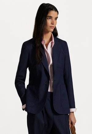 Navy pinstriped blazer made of structured fabric with a notched lapel and single button closure. Paired with a light pink shirt underneath.