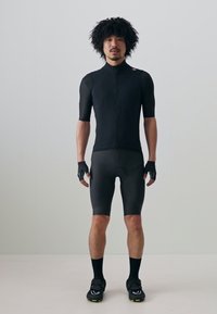 Czarna koszulka kolarska z krótkimi rękawami, dopasowane obcisłe szorty, rękawice i buty kolarskie. Gładki materiał i aerodynamiczny krój sportowy.
