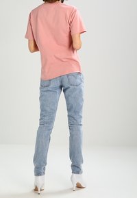 Růžové bavlněné tričko s krátkými rukávy, spárované se světle modrými džíny a bílými vysokými podpatky. Džíny mají klasický pětikapsový design.