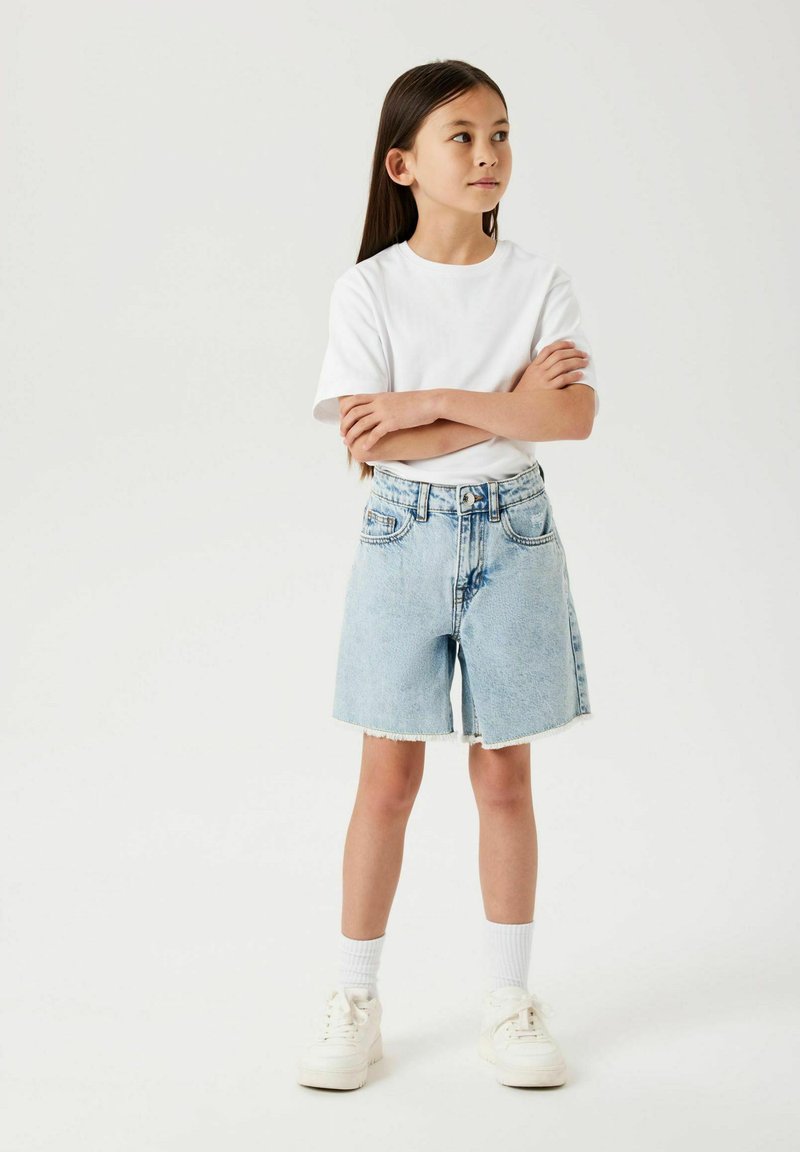 Shorts en denim avec un délavage clair, ourlet effiloché, taille haute et deux poches avant, associés à un t-shirt blanc uni et des baskets blanches.