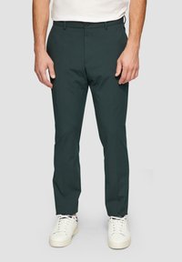 Dunkelgrüne Hose aus glattem Stoff, mit Slim-Fit, flachem Vorderteil und einem einzelnen Knopfverschluss. Kombiniert mit weißen Sneakers.