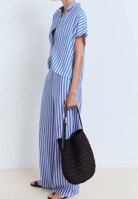 Haut et pantalon assortis rayés bleu et blanc à manches courtes, avec un devant noué. Sac noir en osier avec bandoulière. Sandales.