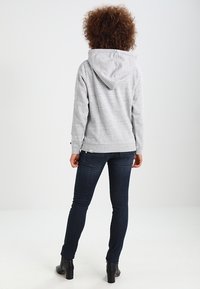 Szara bluza z kapturem na sznurki, wykonana z miękkiego materiału o ciekawej fakturze, w luźnym kroju, zestawiona z ciemnoniebieskimi dżinsami i botkami odkrytymi na kostce.