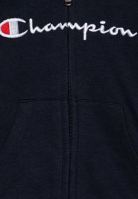 Sudadera con cremallera en color navy, fabricada en un tejido de mezcla de algodón, que presenta una cremallera frontal, dos bolsillos laterales y el logo bordado de "Champion" en blanco y rojo.