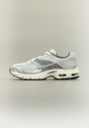 Chaussure de course Nike blanche et grise avec tige en mesh, semelle amortie, design à lacets et unités d'air visibles au talon et à l'avant-pied.