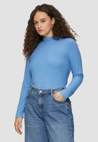 Hellblaues, geripptes Langarmoberteil mit hohem Kragen, kombiniert mit locker sitzenden blauen Jeans aus Denim. Besitzt eine weiche Textur und ein enganliegendes Design.