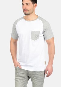 White t-shirt with gray raglan sleeves, featuring a gray pocket on the left chest. Smooth cotton fabric, round neckline, side seam label.