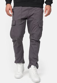 Pantalones cargo grises hechos de un tejido duradero, con múltiples bolsillos laterales y un corte relajado, combinados con zapatillas blancas.